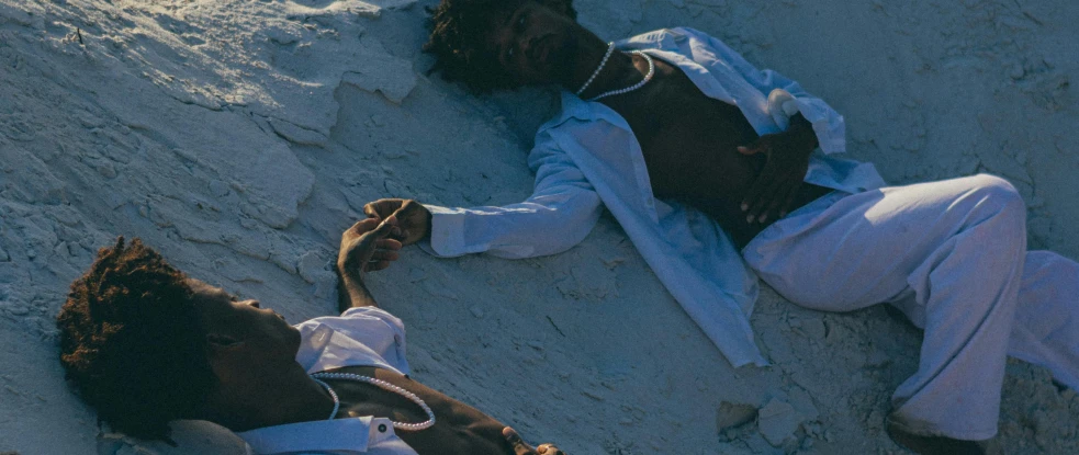 two people wearing clothing laying on the sand