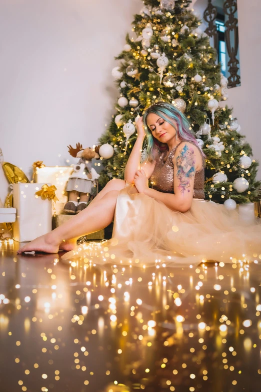 a tattooed woman sits in front of a christmas tree