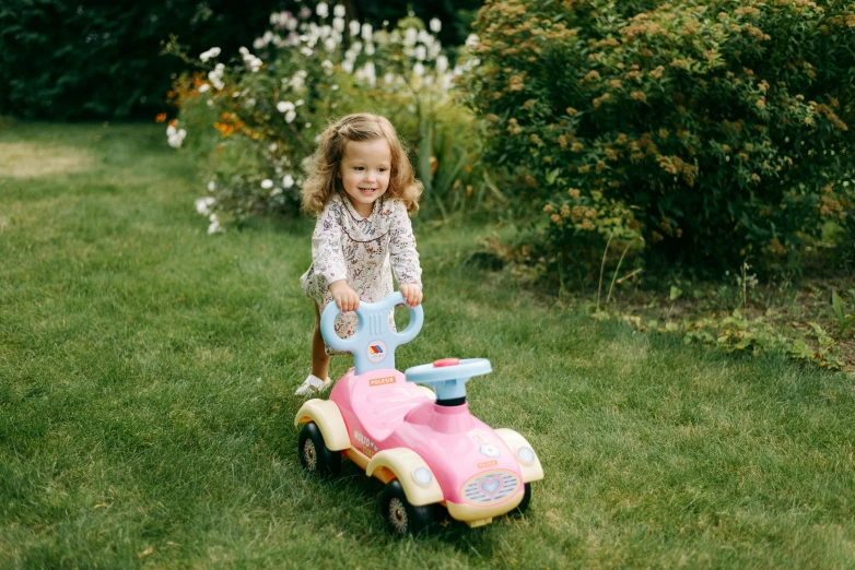 a little girl riding on a pink and blue toy car