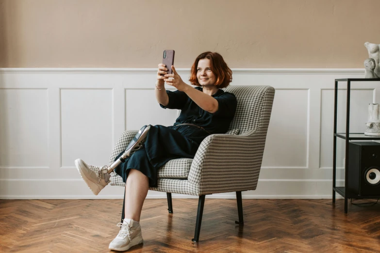 woman in a black dress sitting on a chair taking a selfie