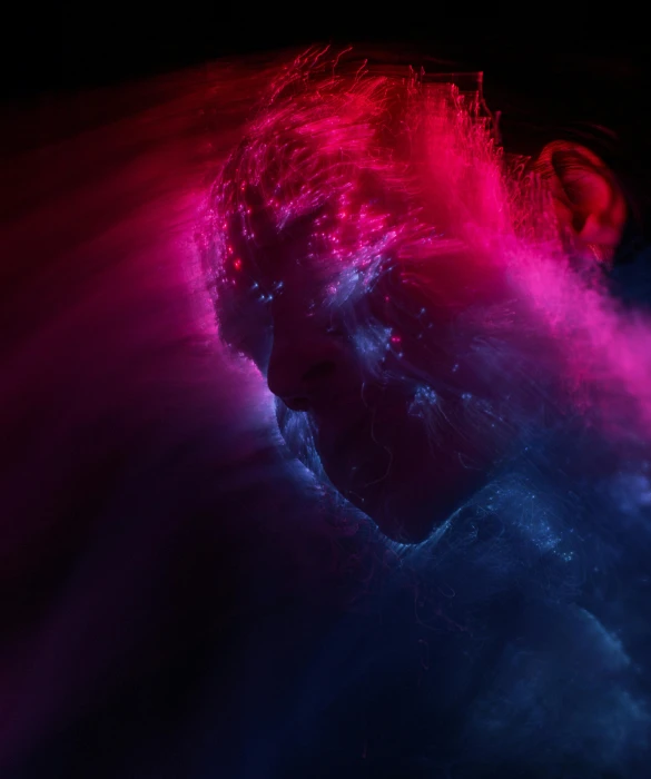 a dark image of the face of a man, with colors being sprayed on it