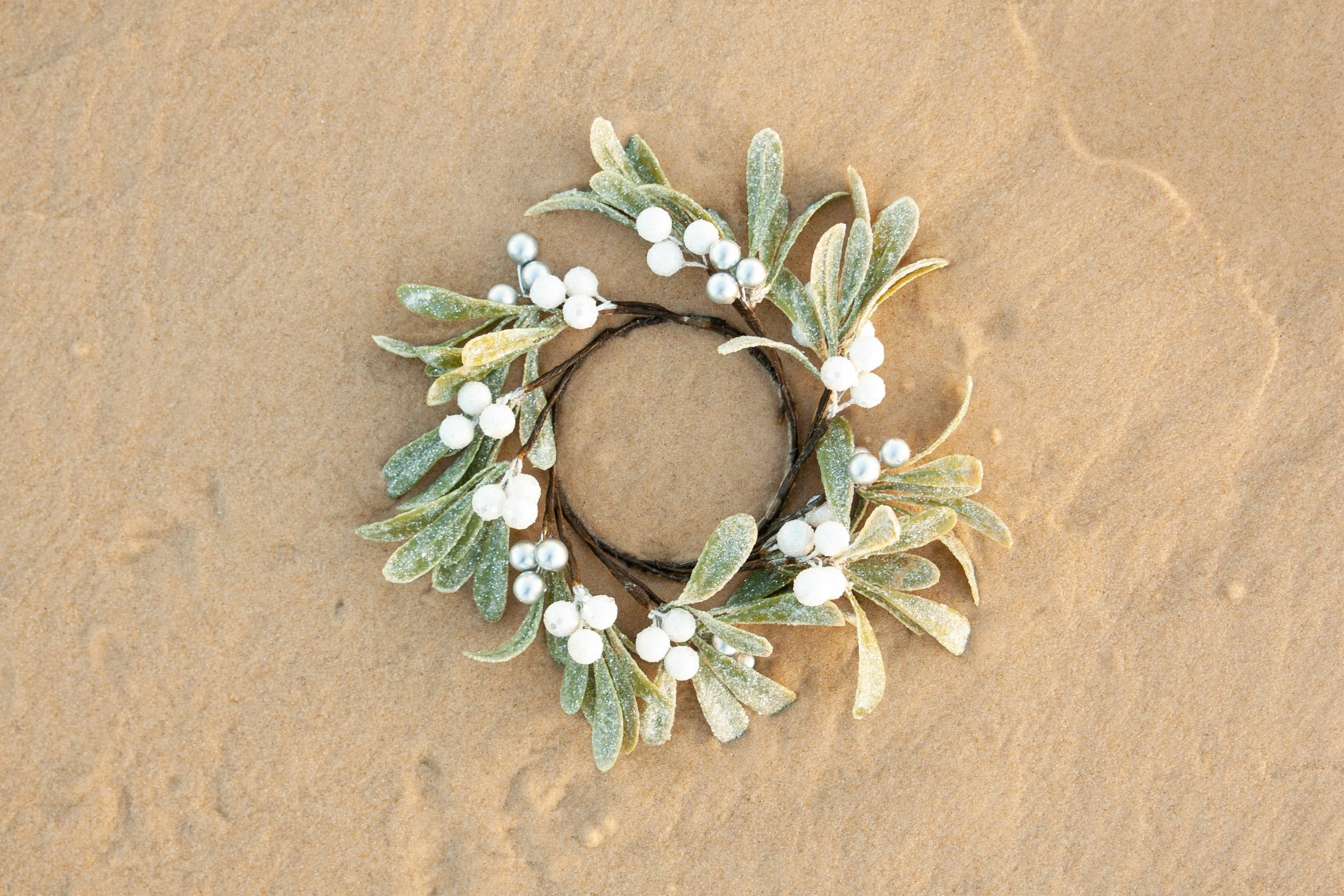 a wreath made from twigs and flowers is lying in the sand