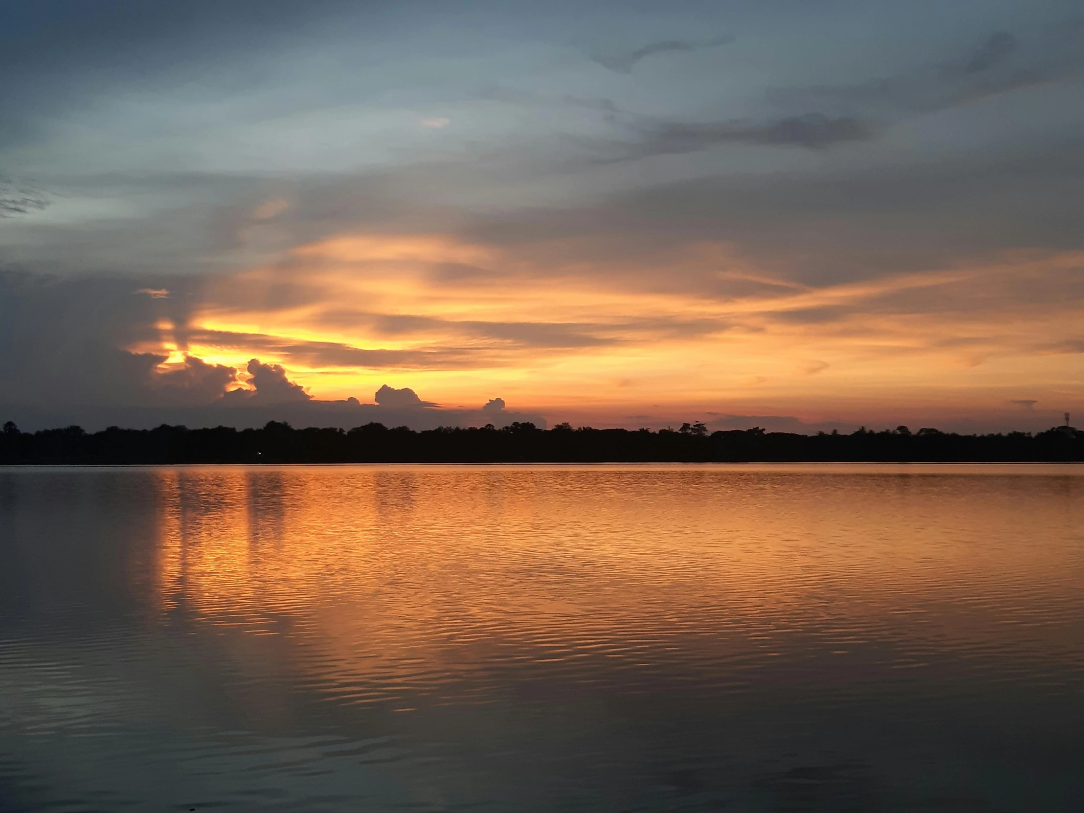 a body of water with clouds and the sun reflecting off the water