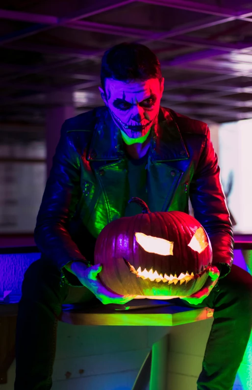 a man holding a lit pumpkin sitting on top of a table