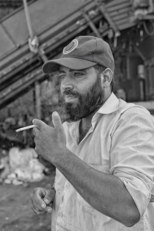 a man with a hat standing and holding a cigarette