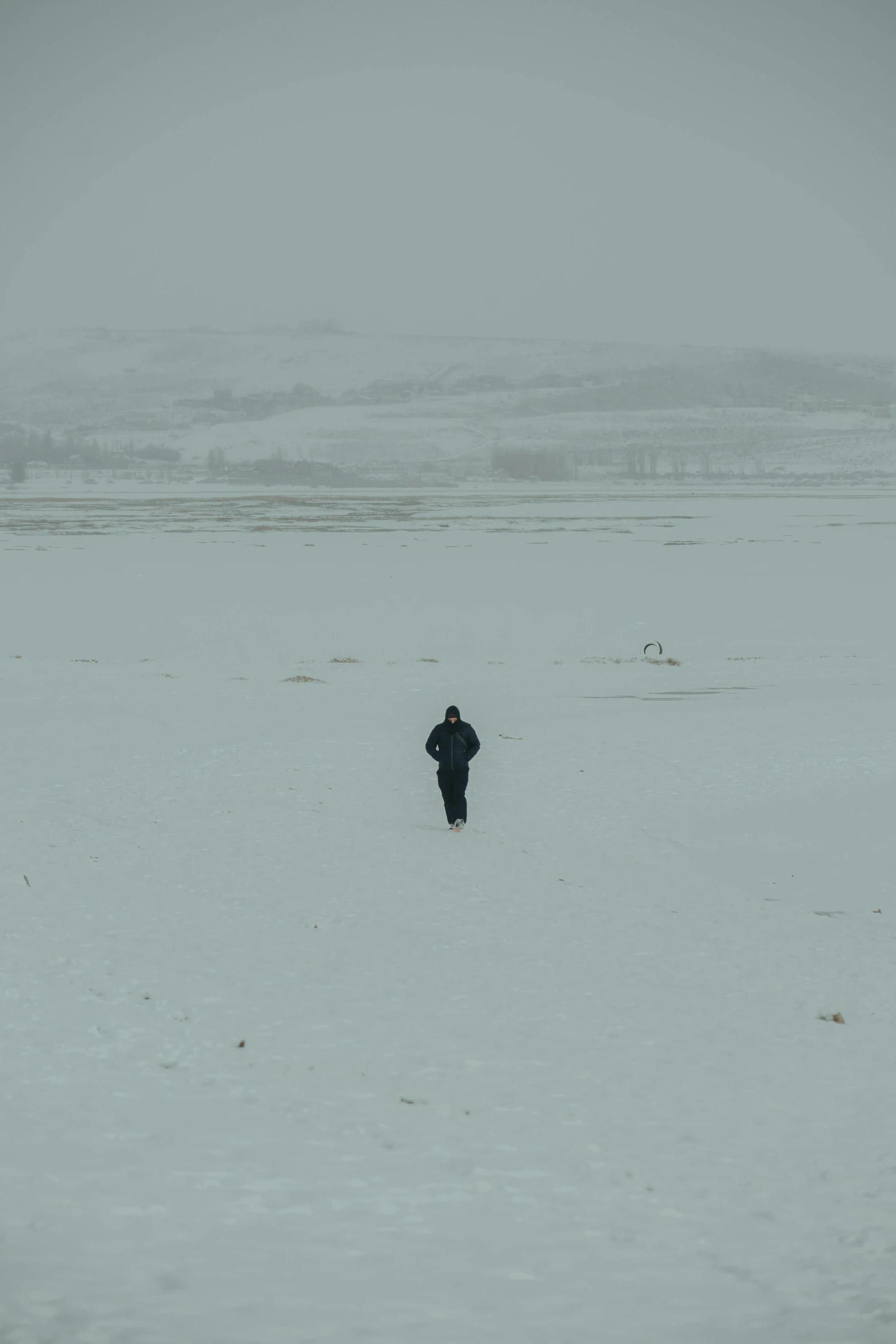 a person standing in snow alone in the middle of an open area