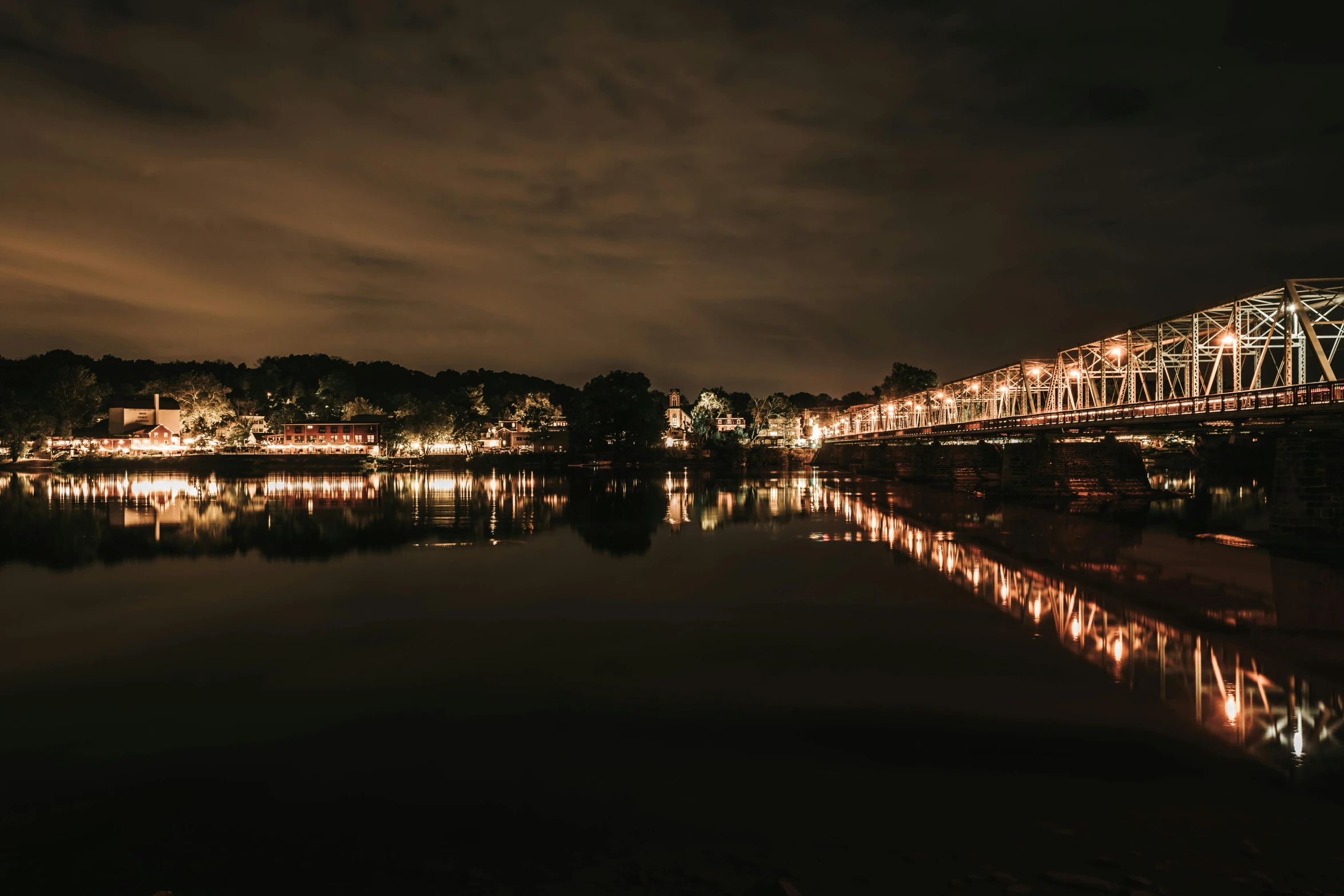 the bridge is lit up at night, reflecting in the water