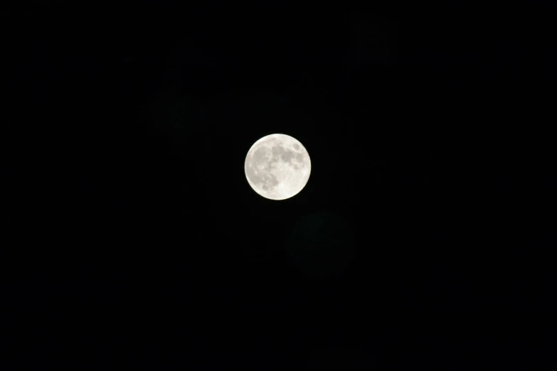 a very full moon is seen in the dark sky