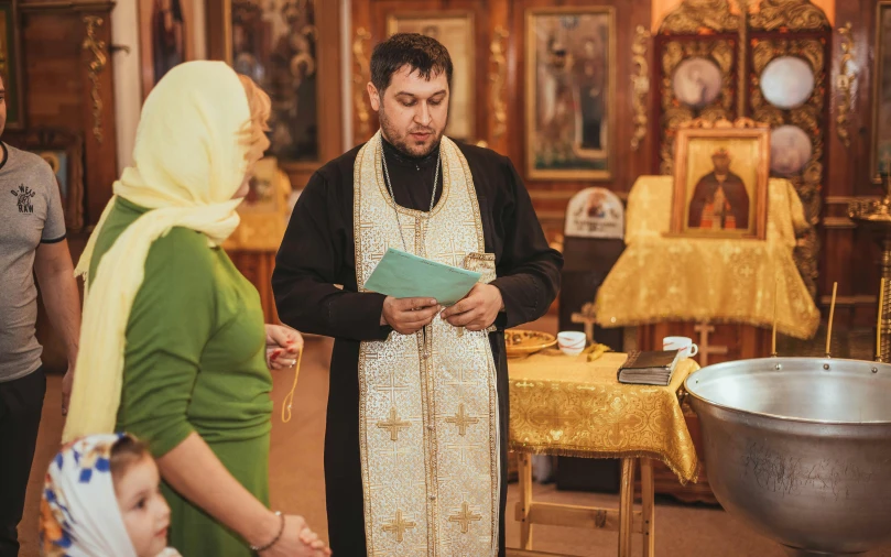 a man wearing an old fashioned vest standing with a nun holding up a folder while people look at him