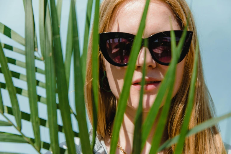 a woman in sunglasses standing behind a leaf