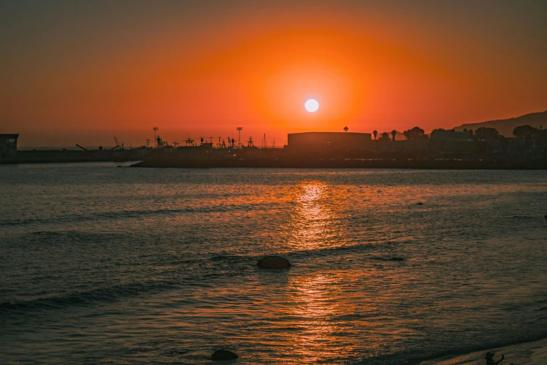 the sun sets over an ocean in a city