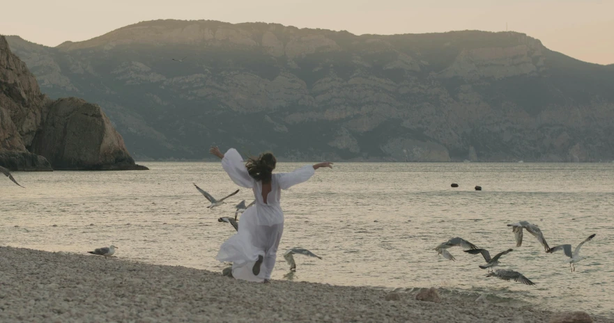 a woman in white dress walking along the beach