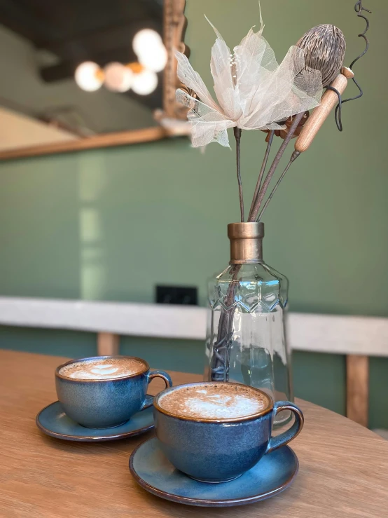 two cups sit on a table near an antique decanter