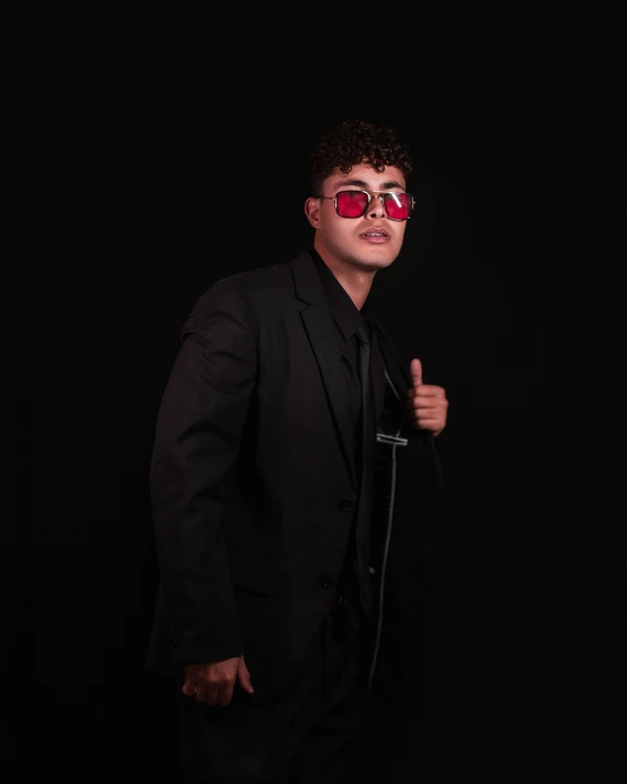 the man in the black suit and red glasses makes the gesture with his hand