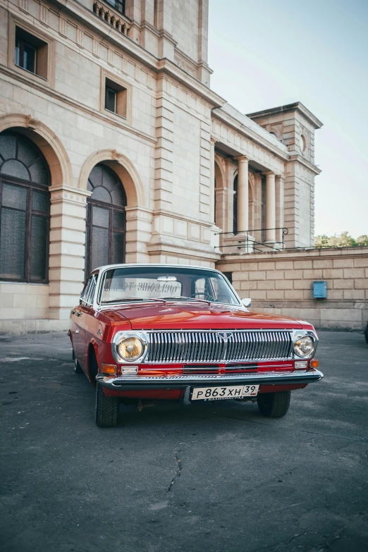 an old red car is parked in front of a building