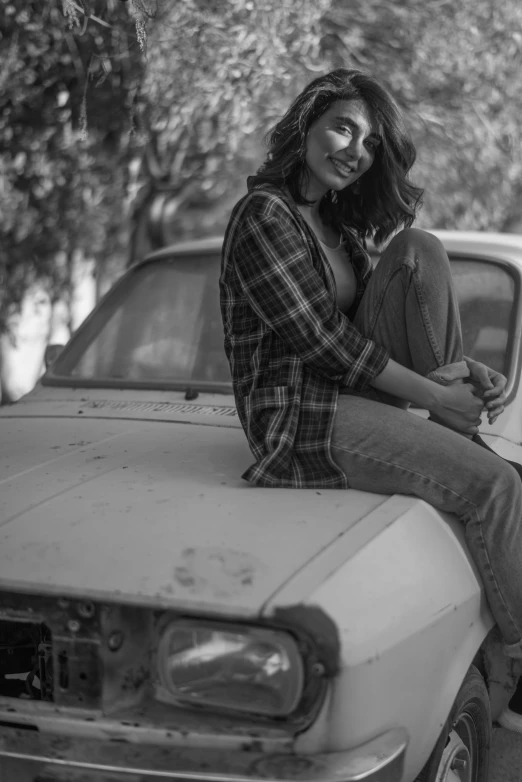 a woman sitting on the hood of a car next to a tree