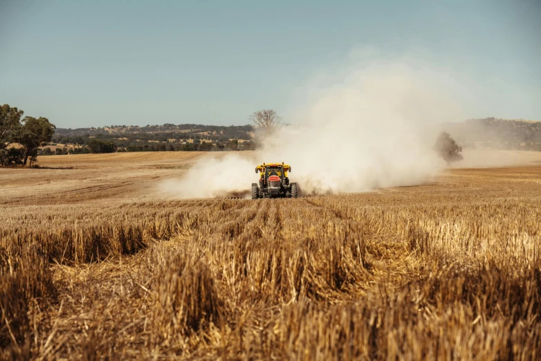 a yellow combine sits in a field that has grass blowing