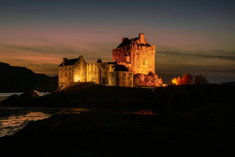 the castle is lit up at night on a hill near a body of water