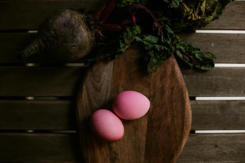 a wood  board topped with three pink eggs