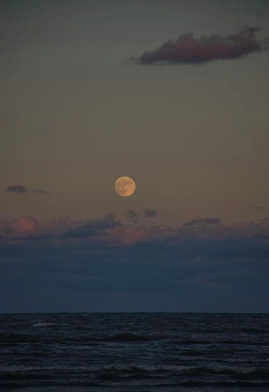 the moon above the water as seen from the shore