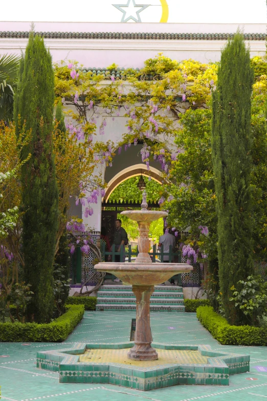 an ornamental fountain surrounded by trimmed bushes and potted trees