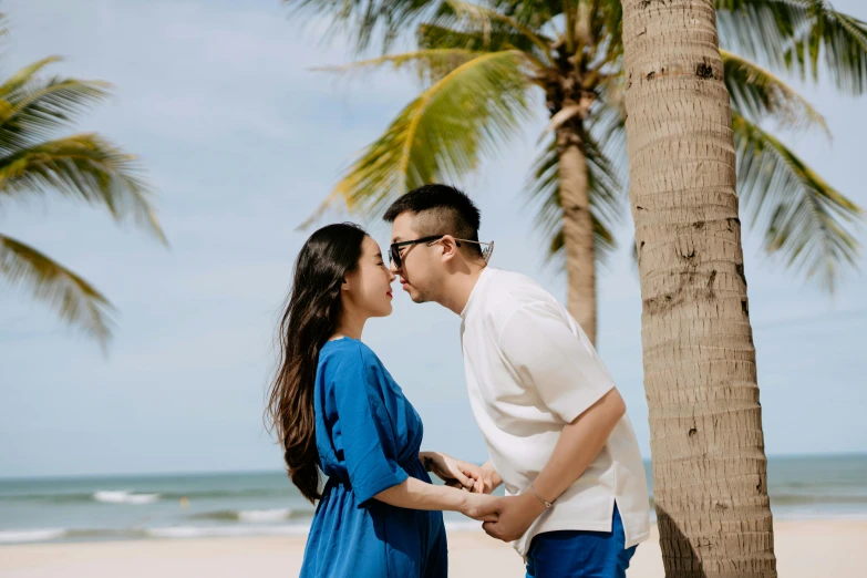 two people standing on the beach next to some trees