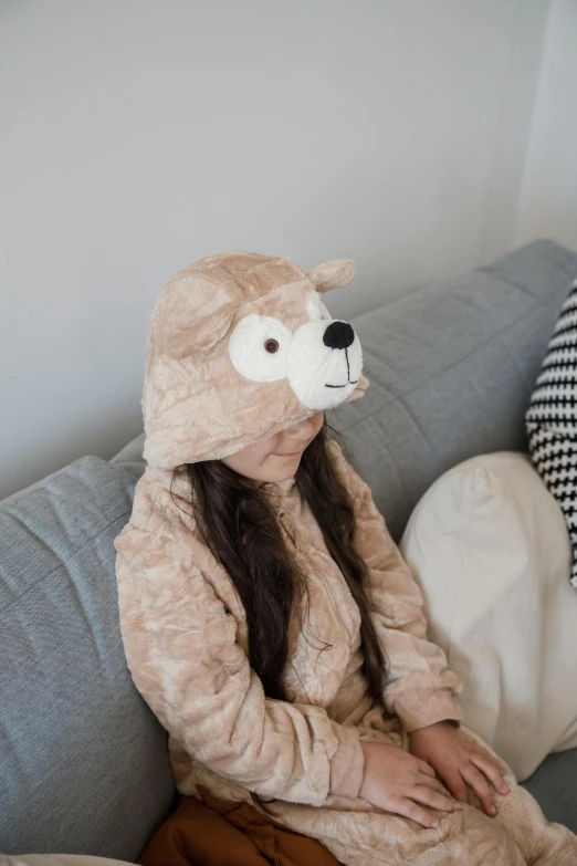 a child sitting on a couch wearing a stuffed bear hat