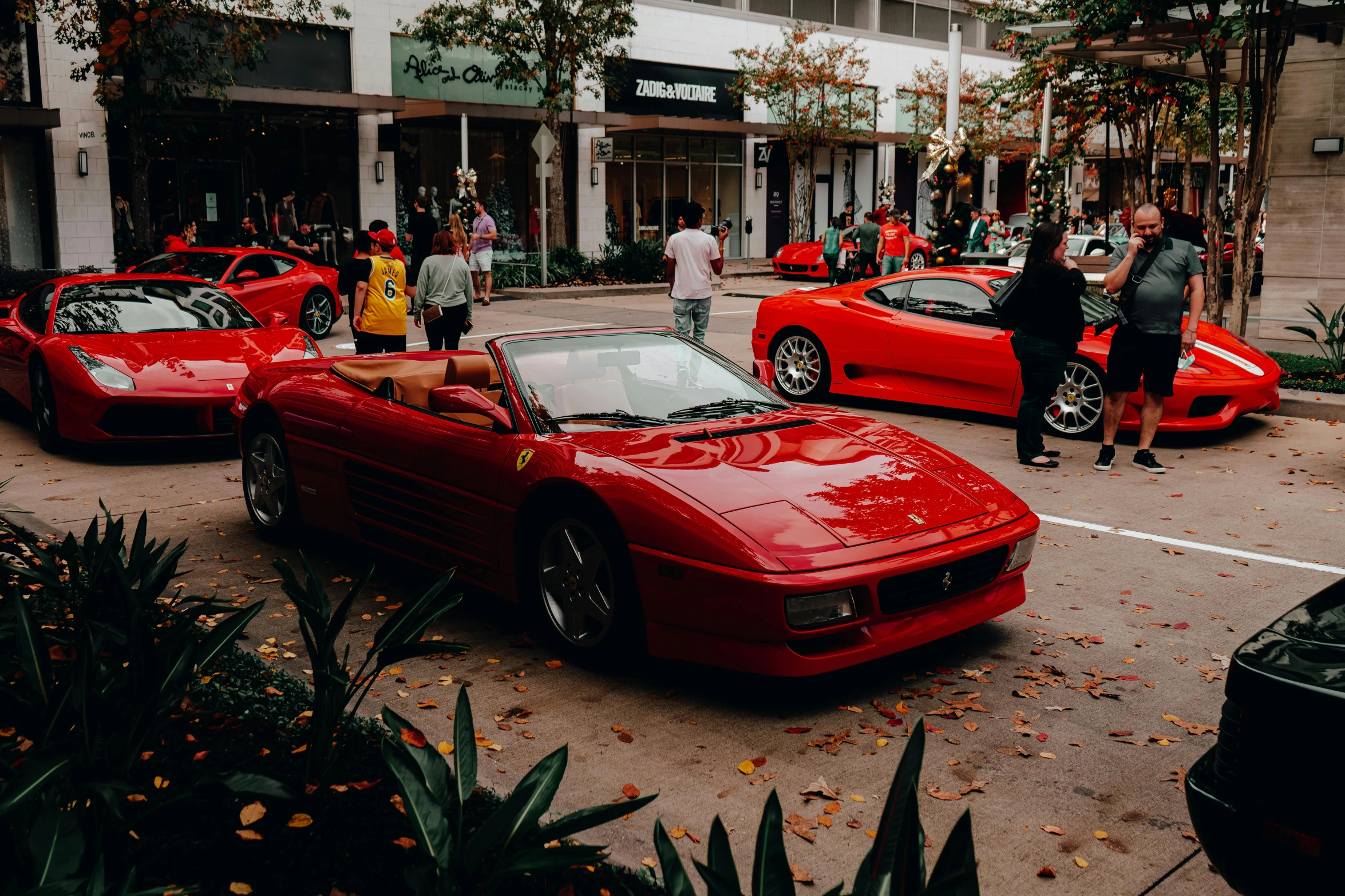 several people standing next to red sports cars in an urban setting