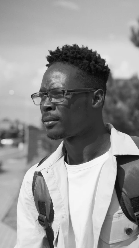 black man with glasses standing by a car looking into the distance