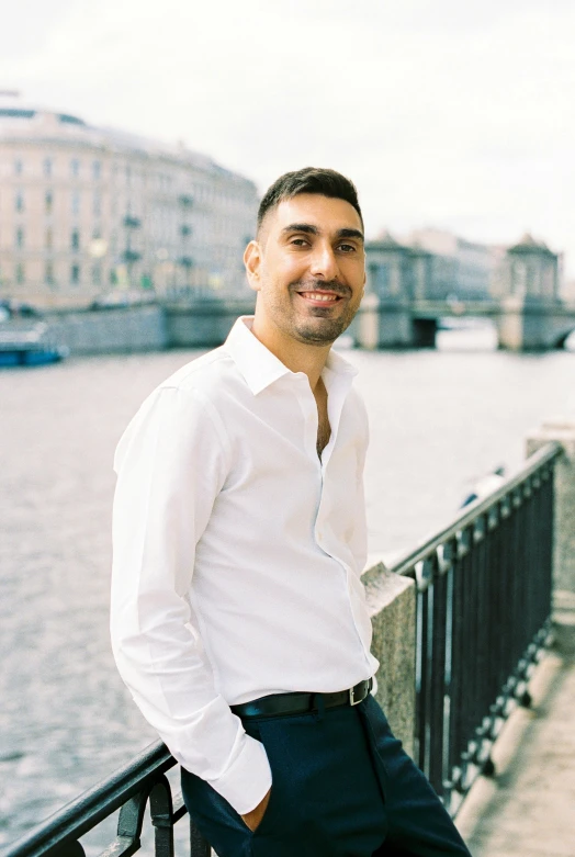 a man in a white shirt and pants leaning against a railing by the water