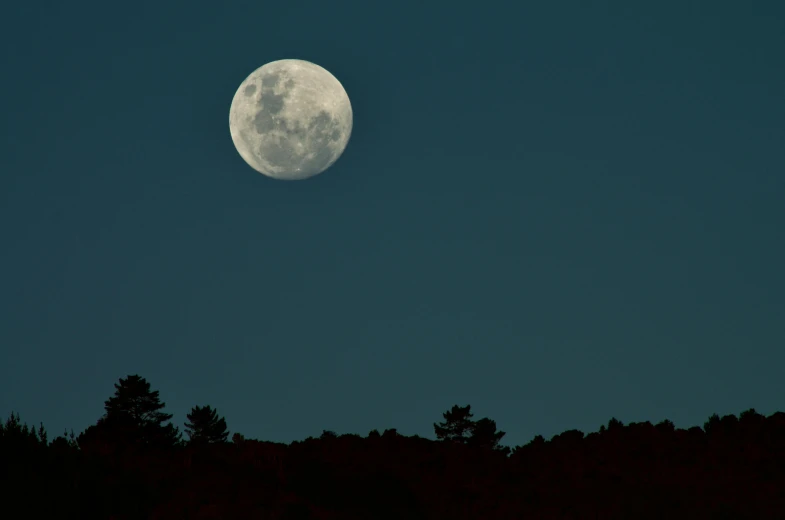 the moon over a dark hillside is silhouetted against the black sky