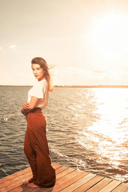 a woman standing on a wooden pier with the sun behind her