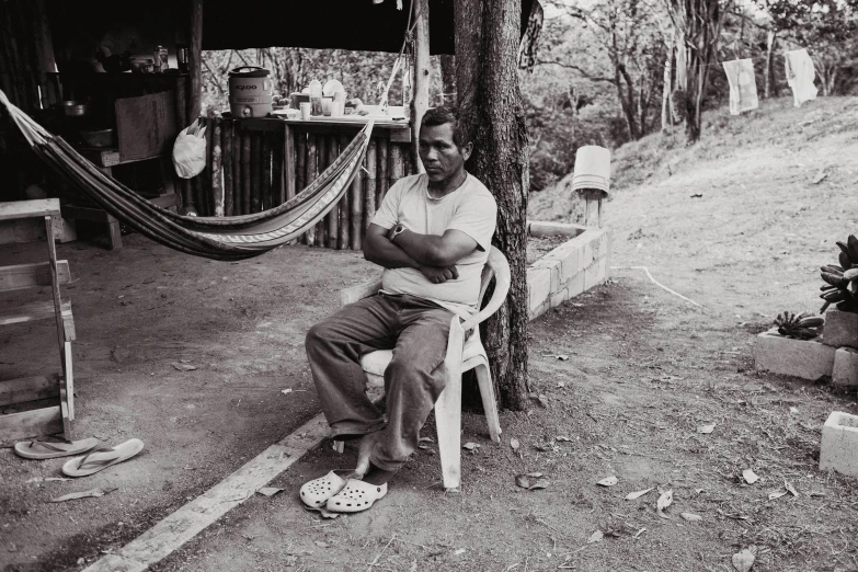 an old man sits in a chair near a tree