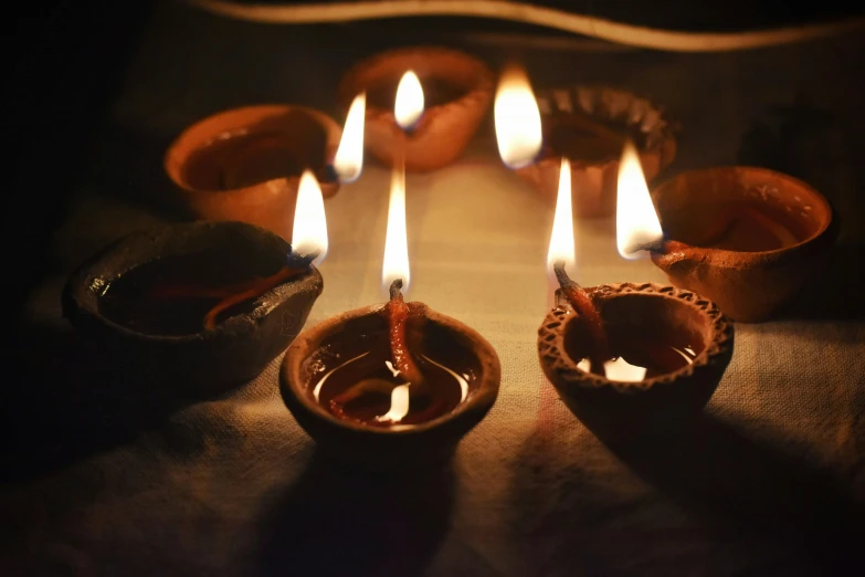 three clay bowls and a lit candle surrounded by smaller ones