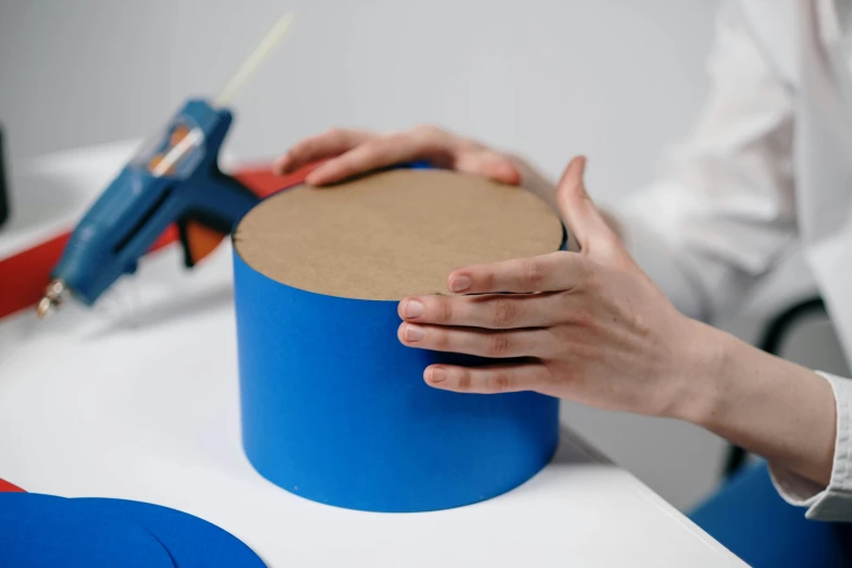 the hand holds the small round cardboard piece near the large object