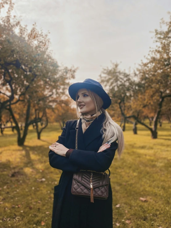 woman in coat and hat with arms crossed standing in field