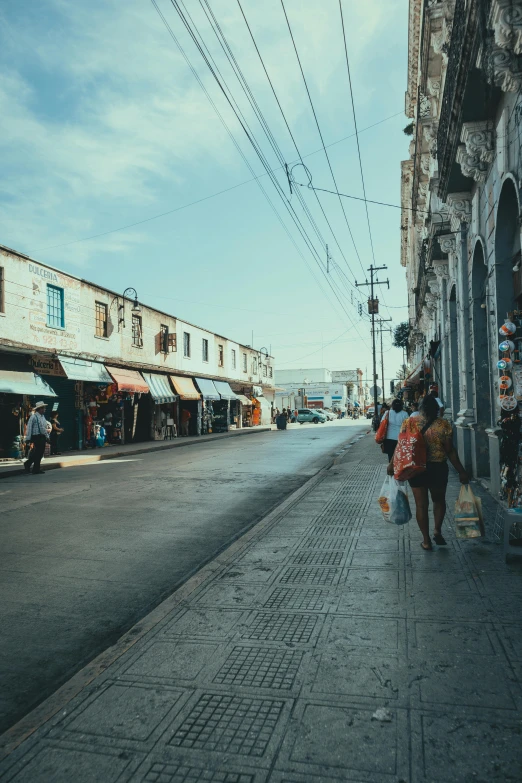 people walking down an empty street with some shops