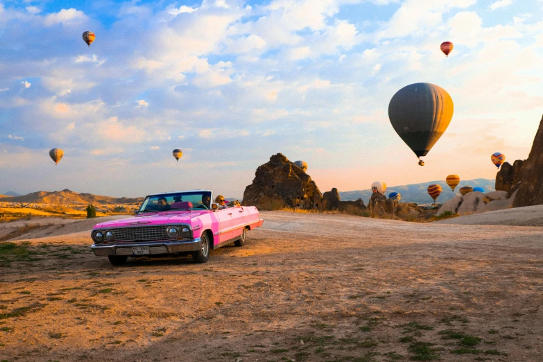 a pink classic is on a dirt road in the middle of a field