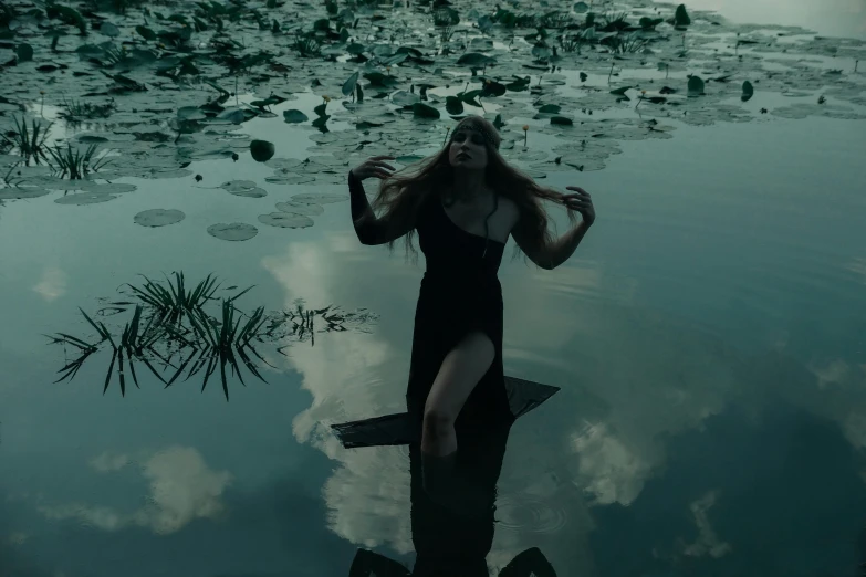 a woman with long hair and an open body walks in the water surrounded by lily pads