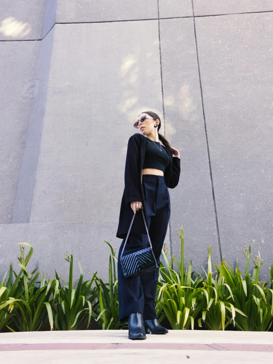 a beautiful woman wearing dark colored clothing standing next to a plant