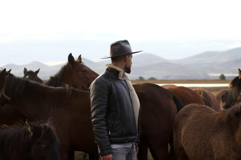 the man is surrounded by many horses in the field