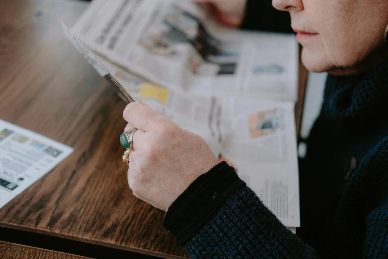 a lady reading the paper with a cell phone in her hand