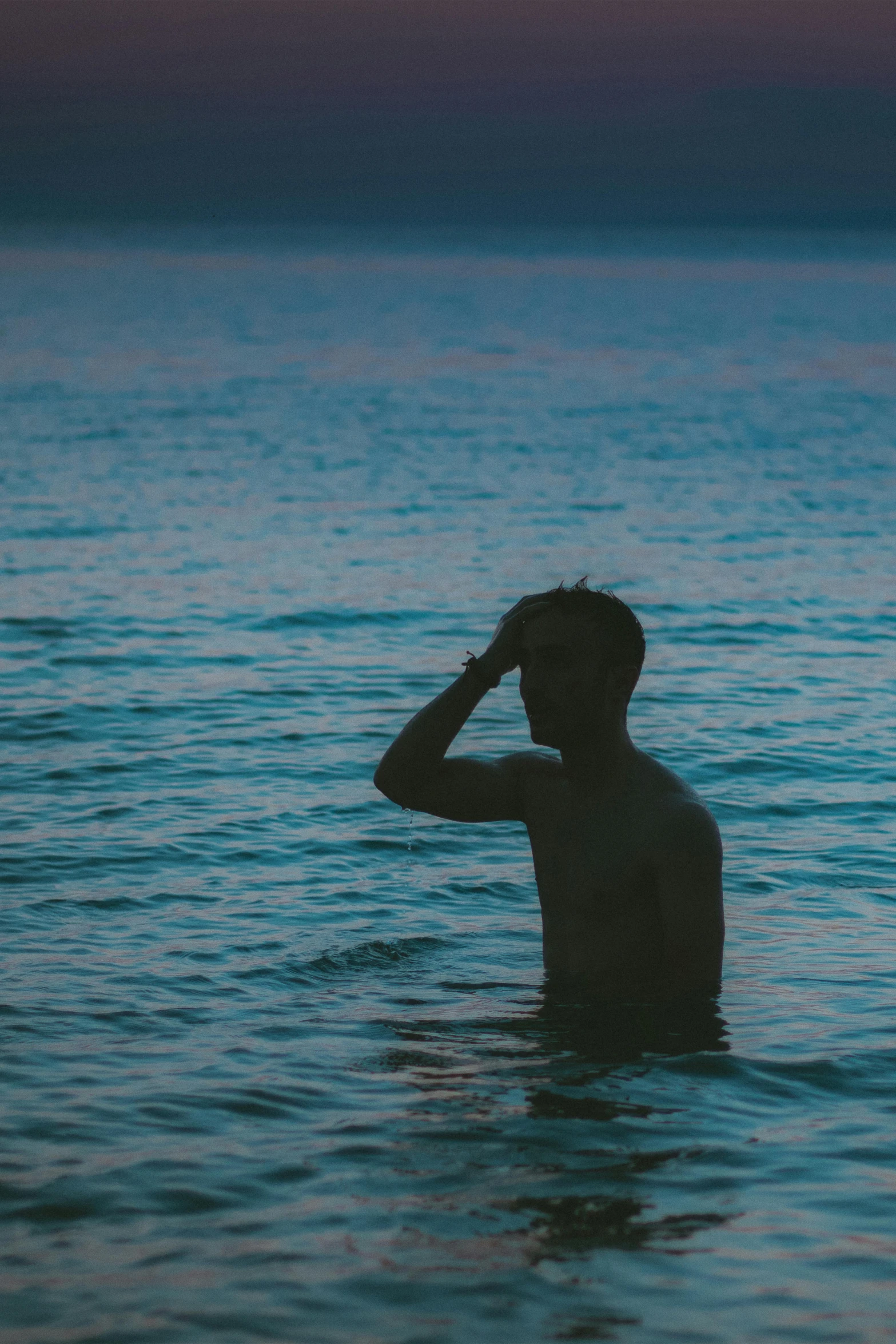 man in water staring to dark sky while holding head with one hand