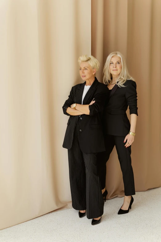 two women in suits and shoes pose for a po