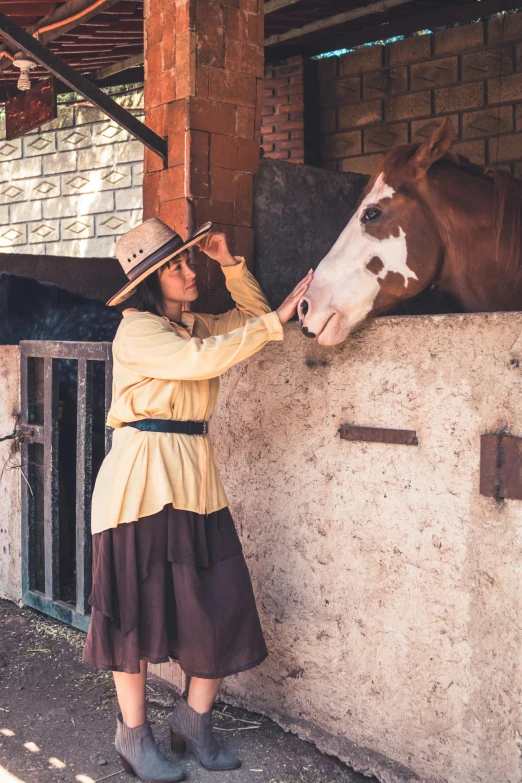 a woman in western wear leaning over to pet a horse