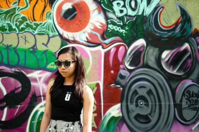 a girl in sunglasses standing in front of graffiti