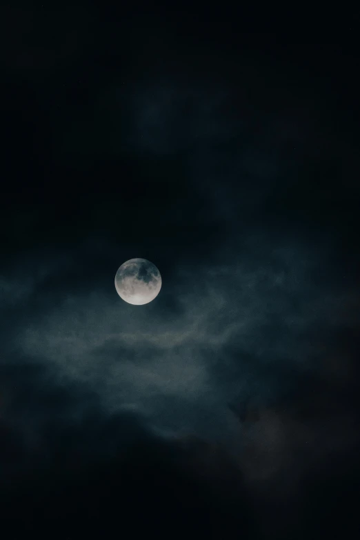 a full moon setting in the cloudy sky