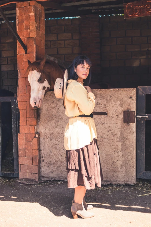 a woman in beige jacket standing next to a horse