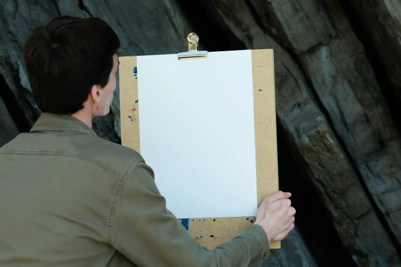 a man holding a white board with clippers next to a tree