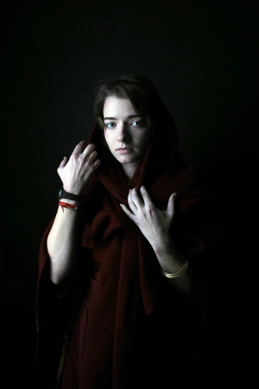 woman in red coat and celets with hands on face looking in camera